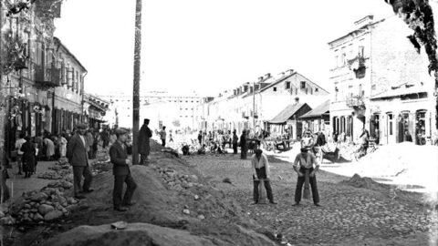 Fragment fotografii archiwalnej z przedstawieniem osób pracujących na ulicy. W tle zabudowa miejska (Siedlce)