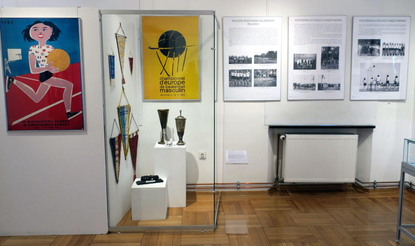 Fragment wystawy z pucharami, pamiątkowymi proporcami oraz plakatem z imprez międzyarowowych zorganizowanych w Polsce.