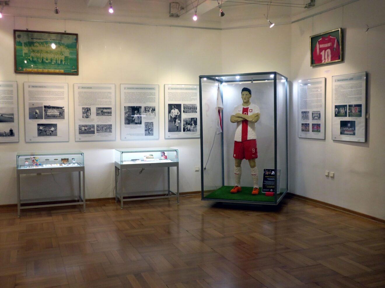 Fragment wystawy z widoczną postacią Robert Lewandowskiego w stroju reprezentacyjnym złożona z kocków lego. Obok fotoramy ze djęciami i gaploty z eksponatami.