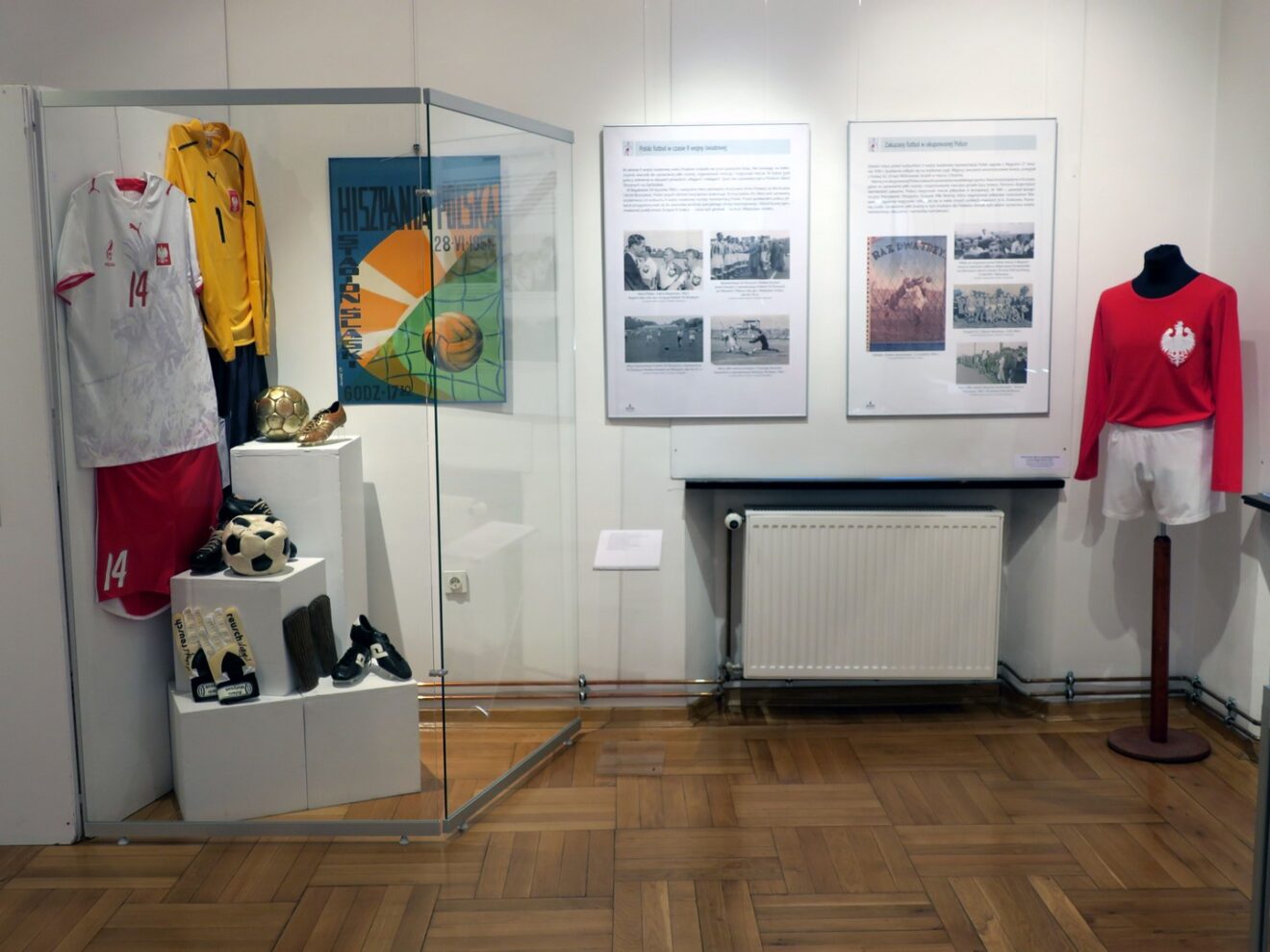 Fragment wystawy prezentujący historyczne akcesoria piłkarskie: kuszuki, rękawice, piłki i buty. Obok fotoramy ze zdjęciami i informacjami.