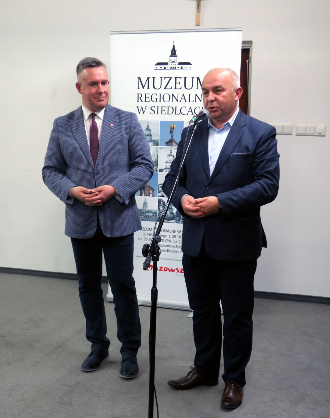 Dwóch mężczyzn ubranych w garnitury stojących przy mikrofonie.