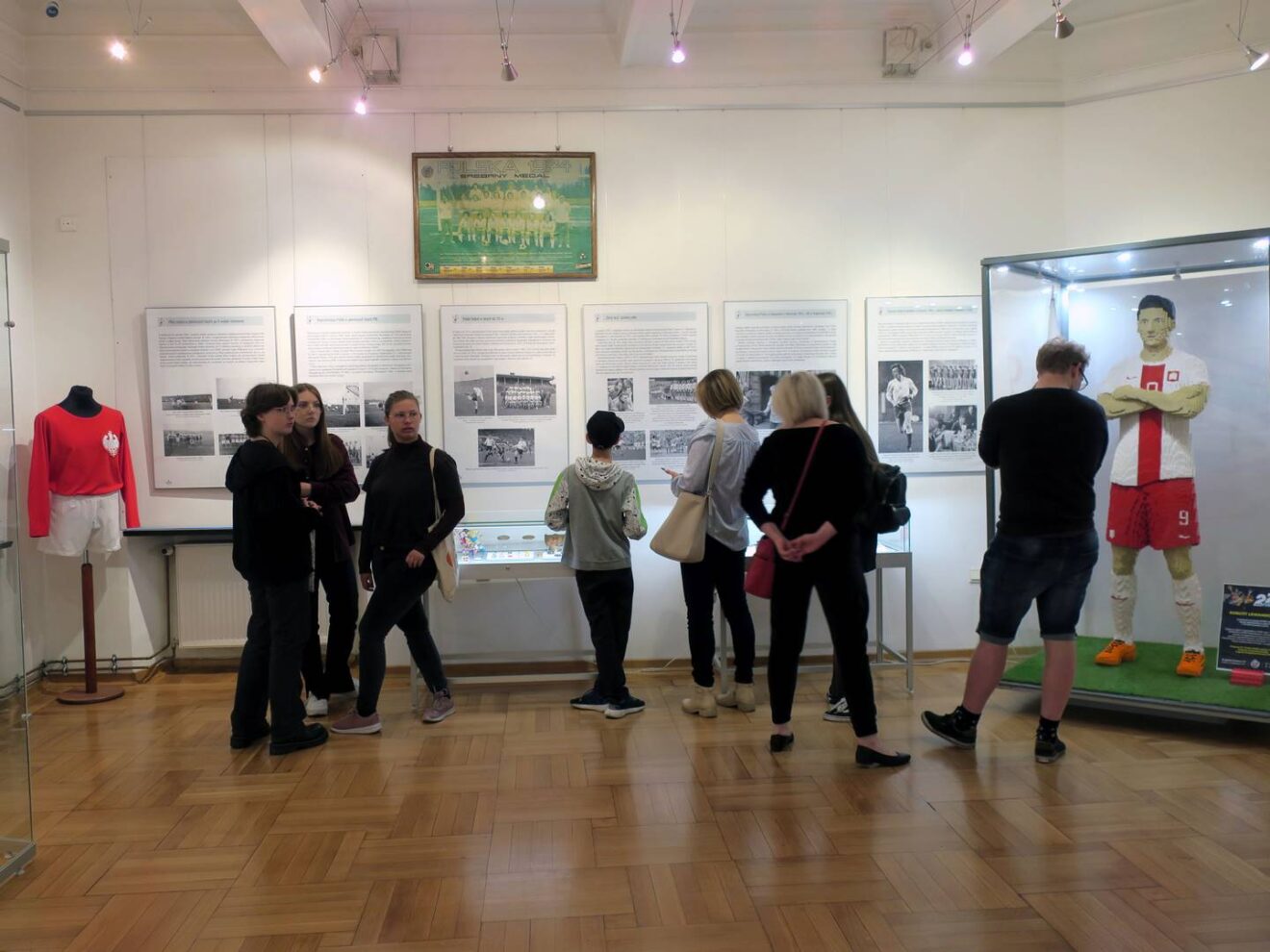 Grupa osób zwiedzająca wystawę o piłce nożnej.