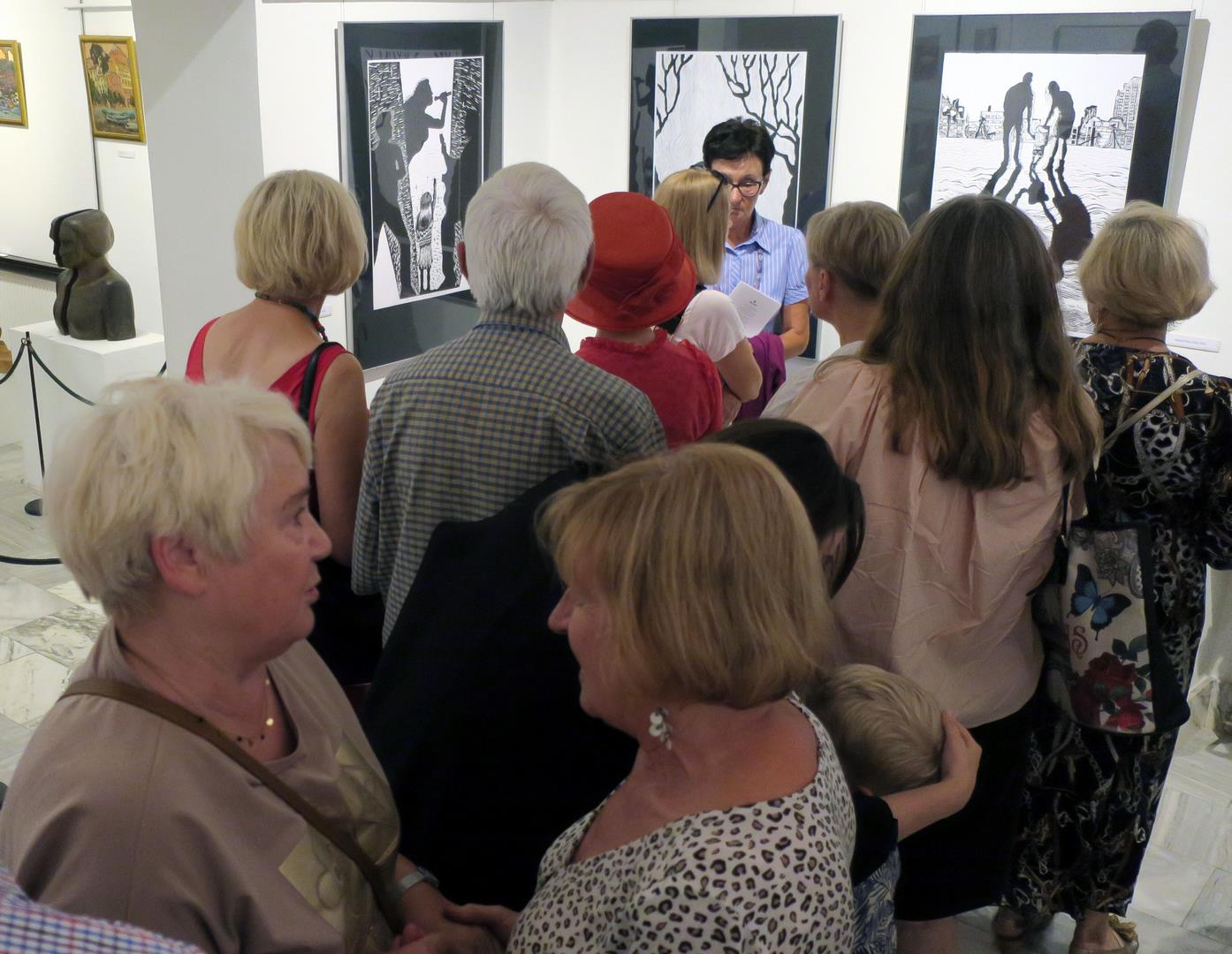 Goście zwiedzający salę ekspozycyjną z powieszonymi na ścianach pracami graficznymi.