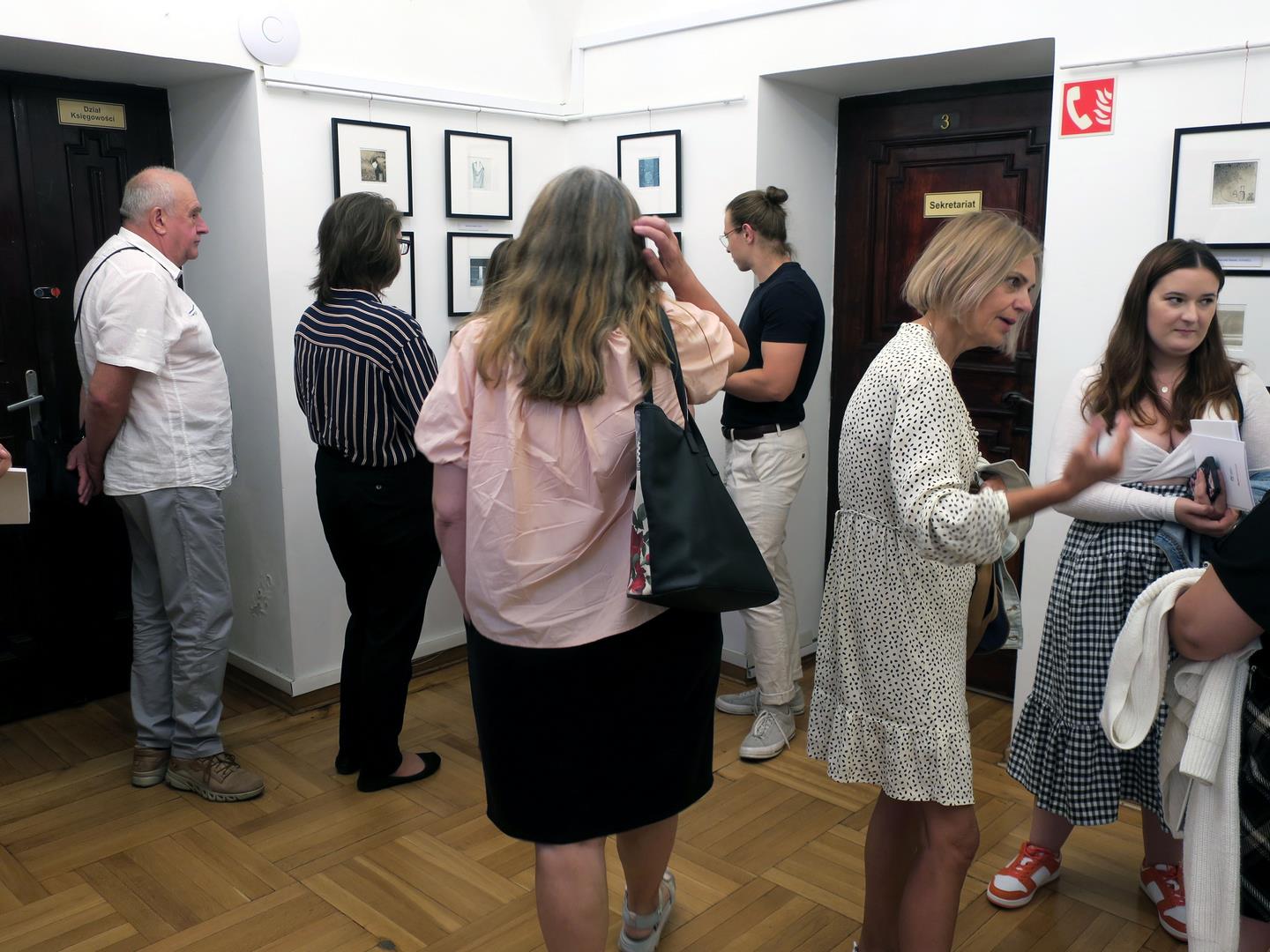 Goście zwiedzający salę ekspozycyjną z powieszonymi na ścianach pracami graficznymi.